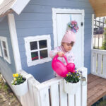 Dziewczynka podlewa kwiatki przy domku ogrodowym