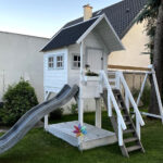 biały domek na podeście ze zjeżdżalnią i huśtawkami