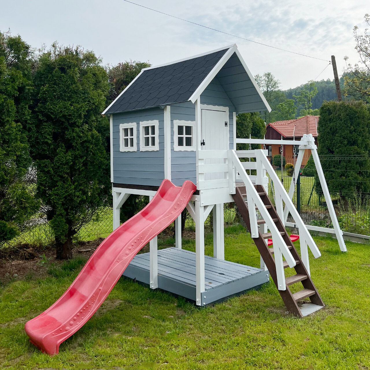 Drewniany domek ogrodowy na podeście dla dzieci ze zjeżdżalnią, huśtawkami i piaskownicą