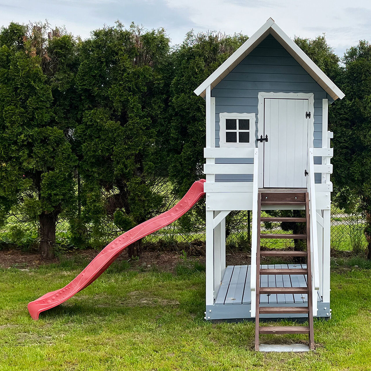 Szary domek drewniany na platformie z czerwoną ślizgawką